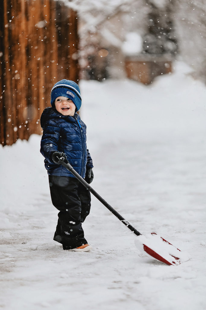 toddler smiling with snow shovel in the snow